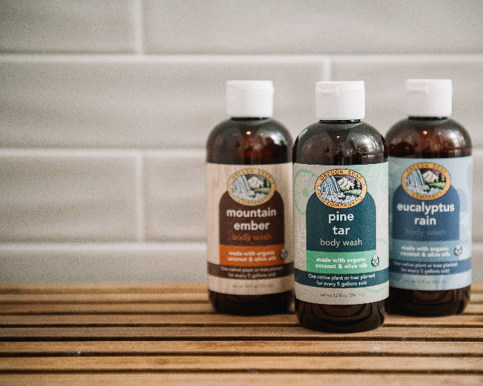 Three bottles of natural body wash with labels on a wooden surface against a tiled wall background.